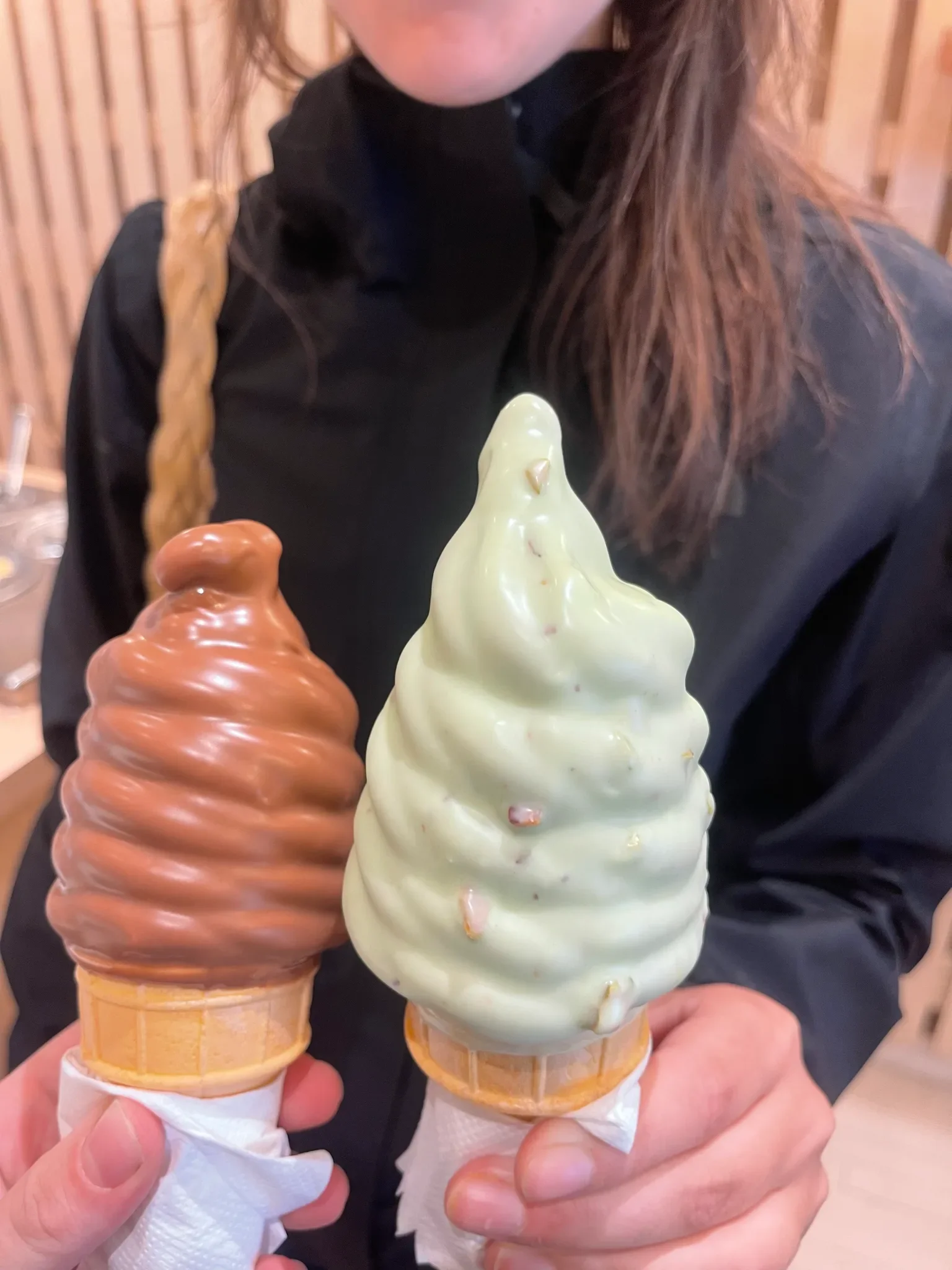 Deux cornets de crème glacée molle trempée, tenus côte à côte : l'un enrobé de chocolat, l'autre d'un glaçage vert pistache parsemé d'éclats.